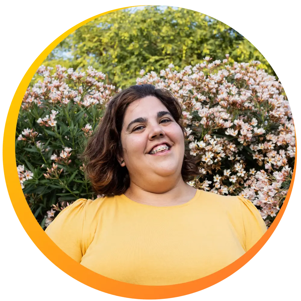 A woman smiling while standing outside against a flower bush
